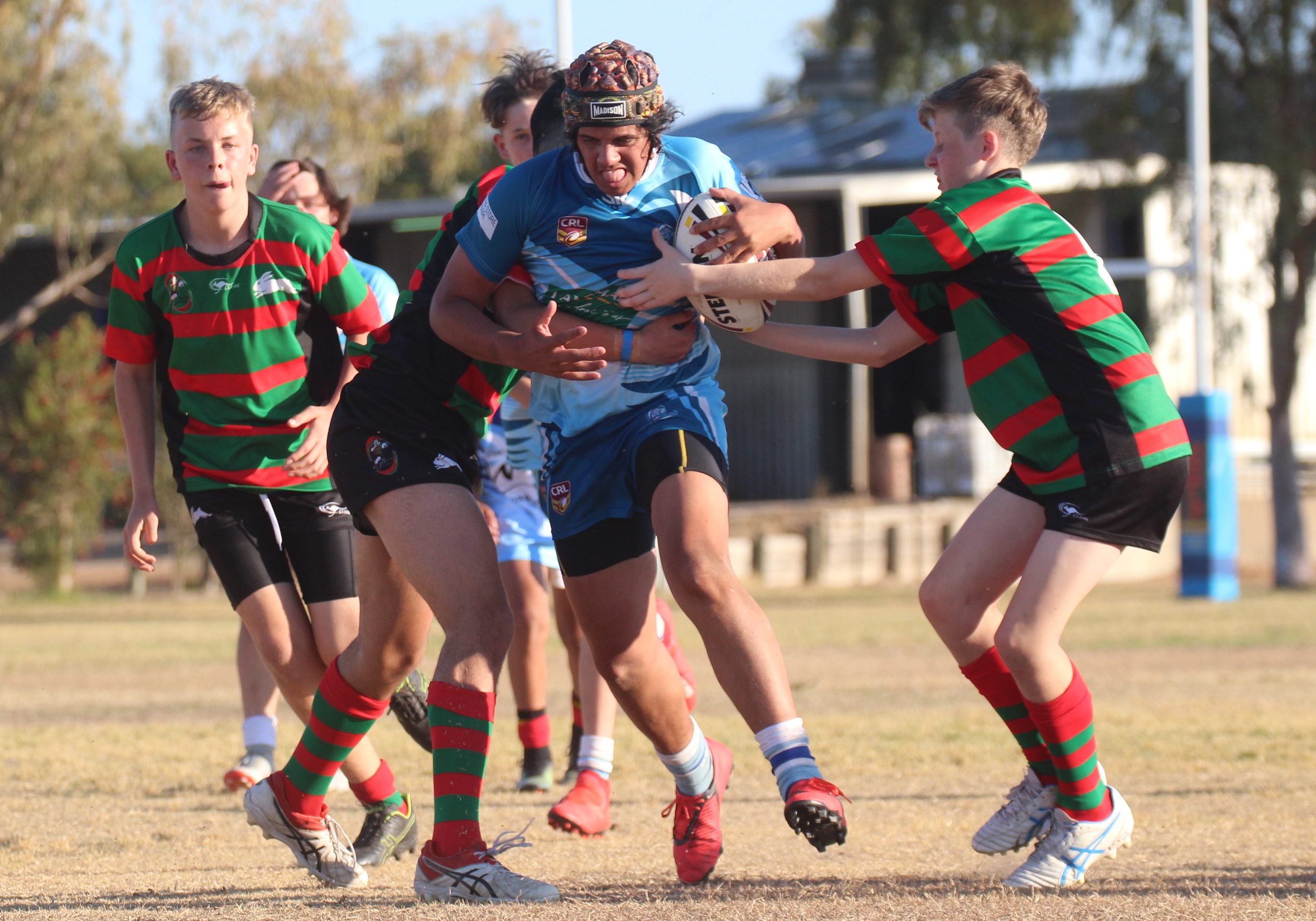 Riley Lamb charges forward as he attempts to break the tackle of two South Sydney defenders.