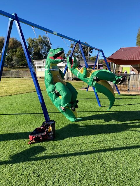 Two dinosaurs playing on the swingset at G.S. Kidd.