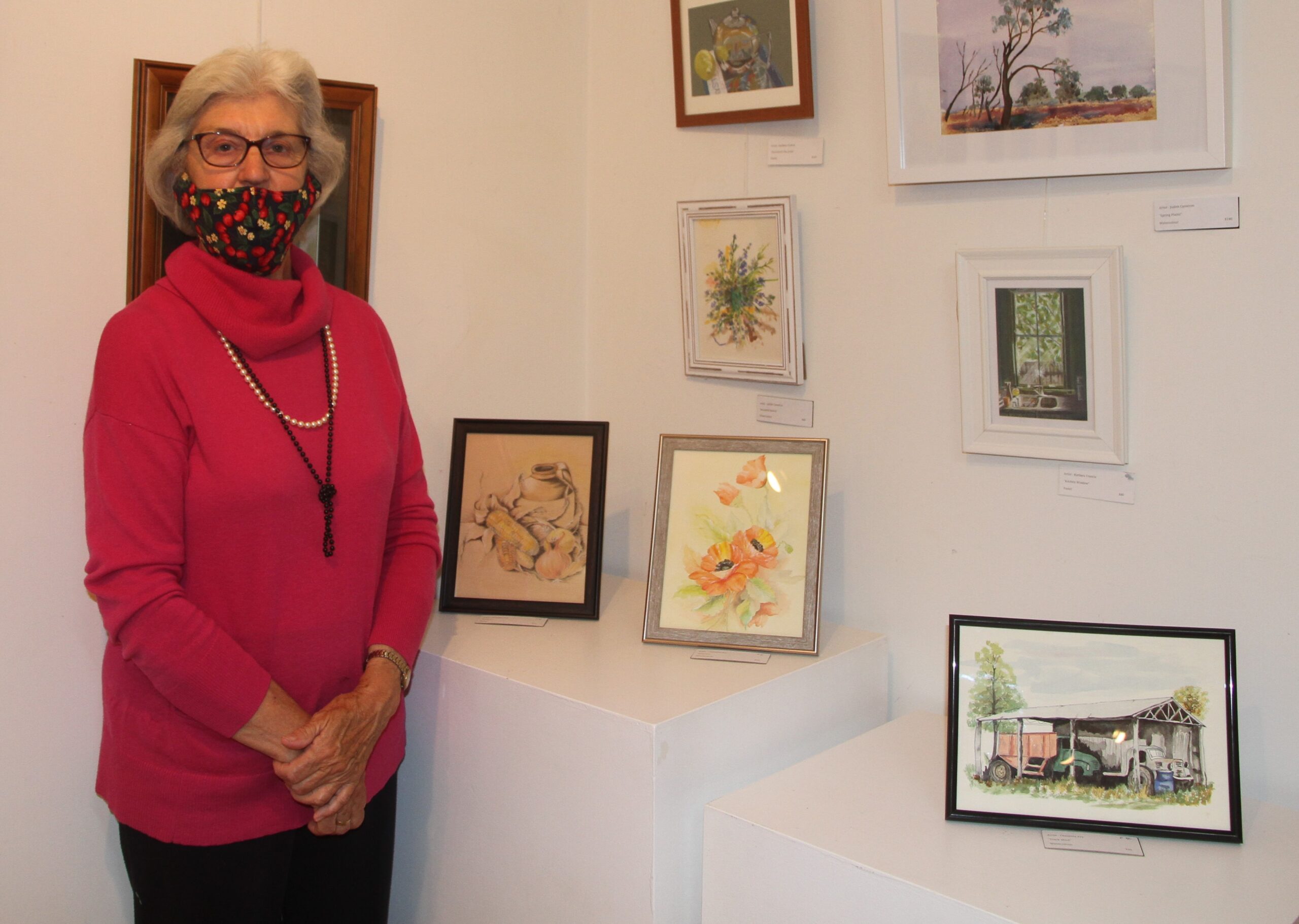 Christine Fry with three paintings (standing on display plinths), from left, ‘Kitchen’ pastels, ‘Flowers’ watercolour, ‘Track Shed’ watercolour.